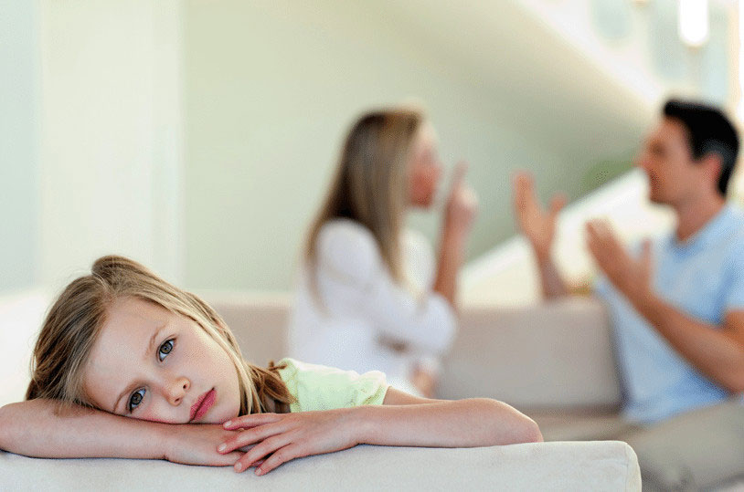 An upset girl on the couch and her parents are fighting in the background.